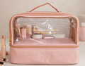 Pink travel makeup bag with clear top compartment holding makeup, front view